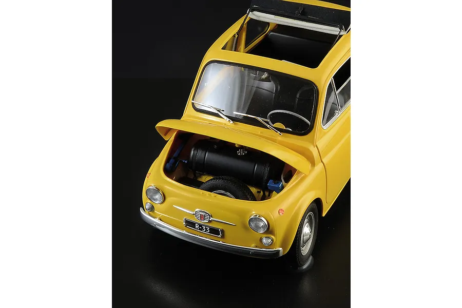 High-angle view of a yellow Italeri 1/12 scale Fiat 500 F model car with its front trunk open, revealing the spare tire and fuel tank.