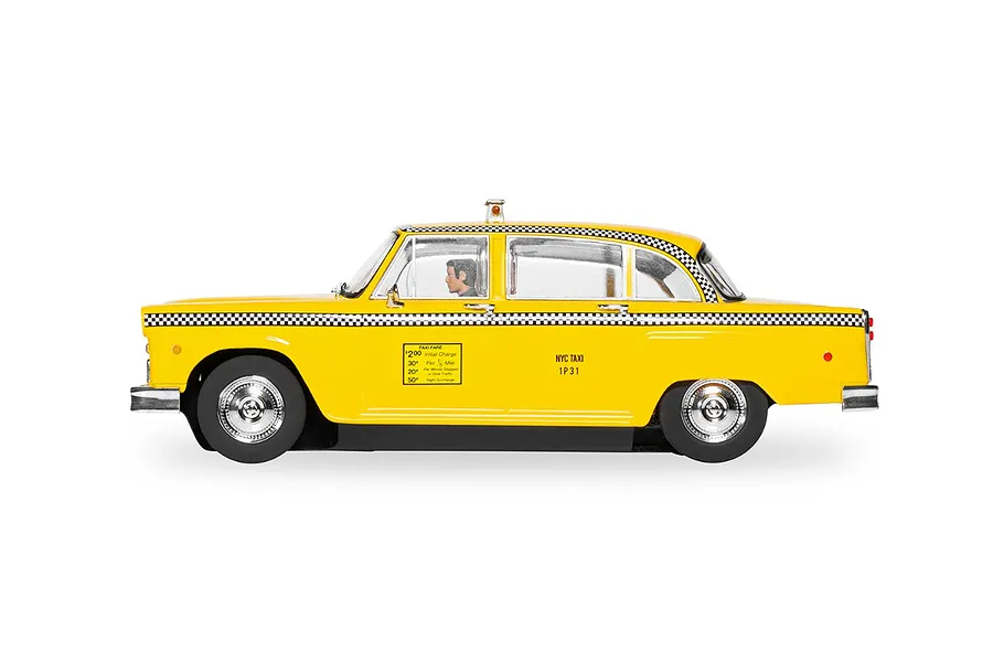 Side view of a 1/32 scale yellow NYC taxi slot car with checkered trim and a driver figure, set against a white background.