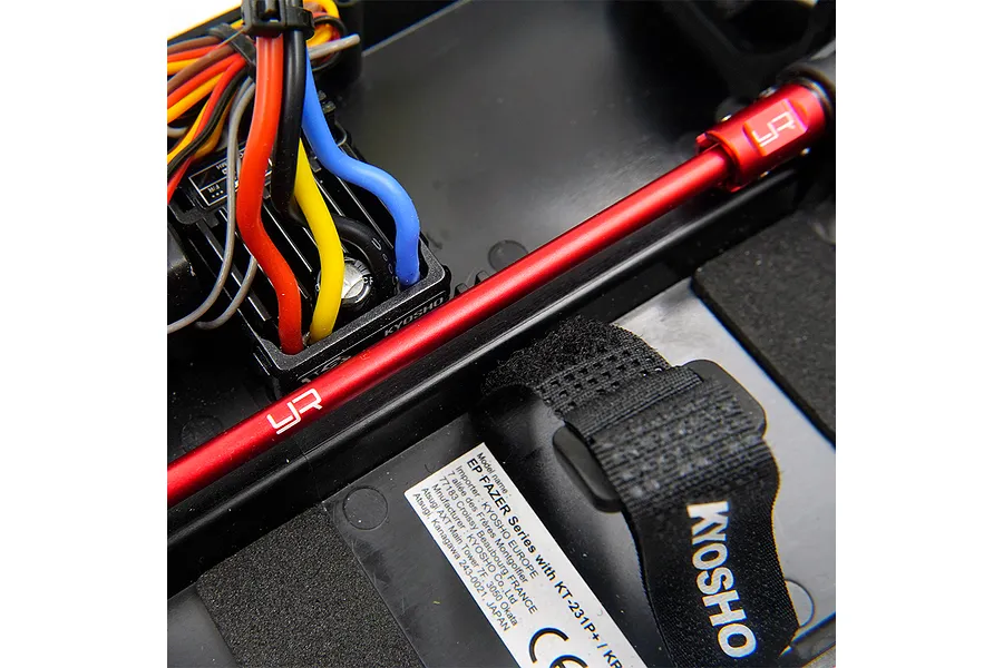A close-up view of a red aluminium driveshaft installed in a Kyosho RC car chassis, featuring the Yeah Racing logo.