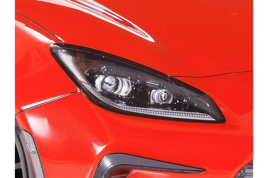 Close-up of the front headlight and red bodywork of a Tamiya Toyota GR 86 RC car model.