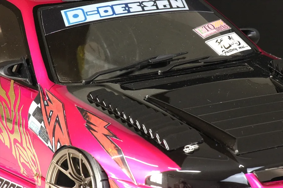 Close-up of a pink RC car body shell featuring black windscreen wipers, hood vents, and various racing decals on the windshield.