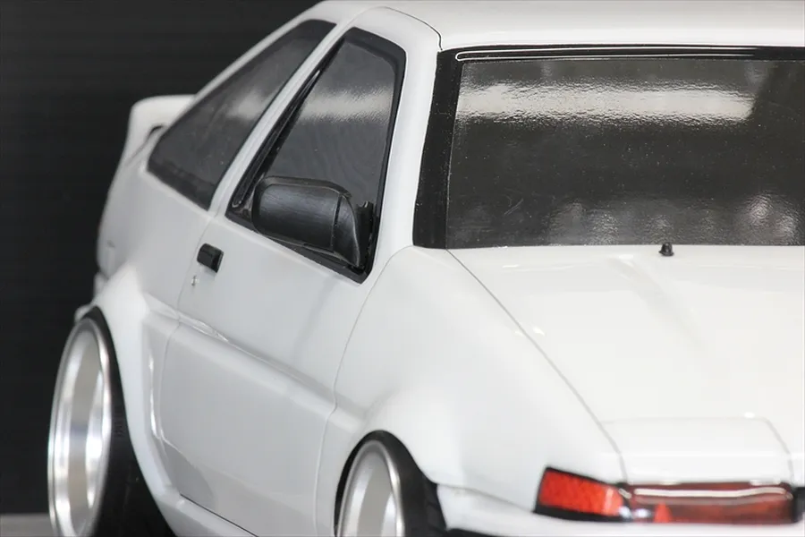 A close-up of a white 1/10 scale RC AE86 model car body, highlighting the black side door mirror attached to the driver's side door.