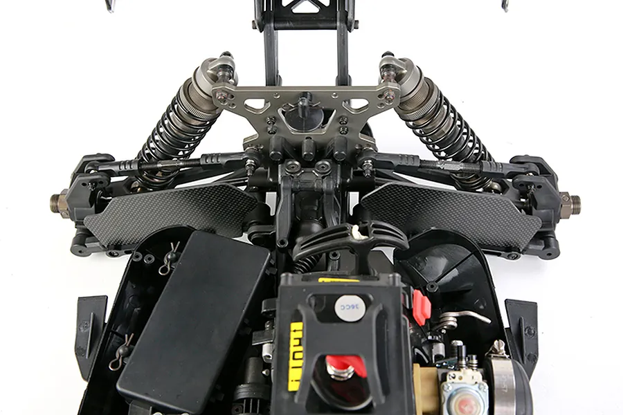 Top-down view of an RC car chassis showing carbon fibre front suspension arm guards installed.