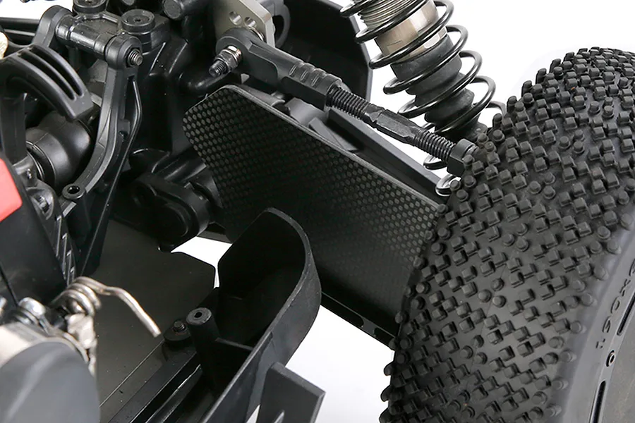 Close-up of a carbon fibre front suspension arm guard installed on an RC buggy, showing the textured plate mounted near the wheel and shock absorber.