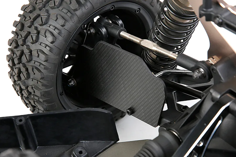 A close-up view of a carbon fibre rear suspension arm guard installed on an RC car, showing the weave pattern and mounting hardware.
