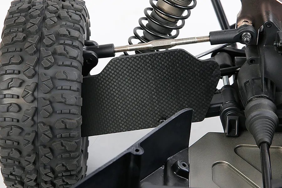 Close-up of a carbon fibre rear suspension arm guard installed on an RC vehicle, showing the weave pattern and mounting position.