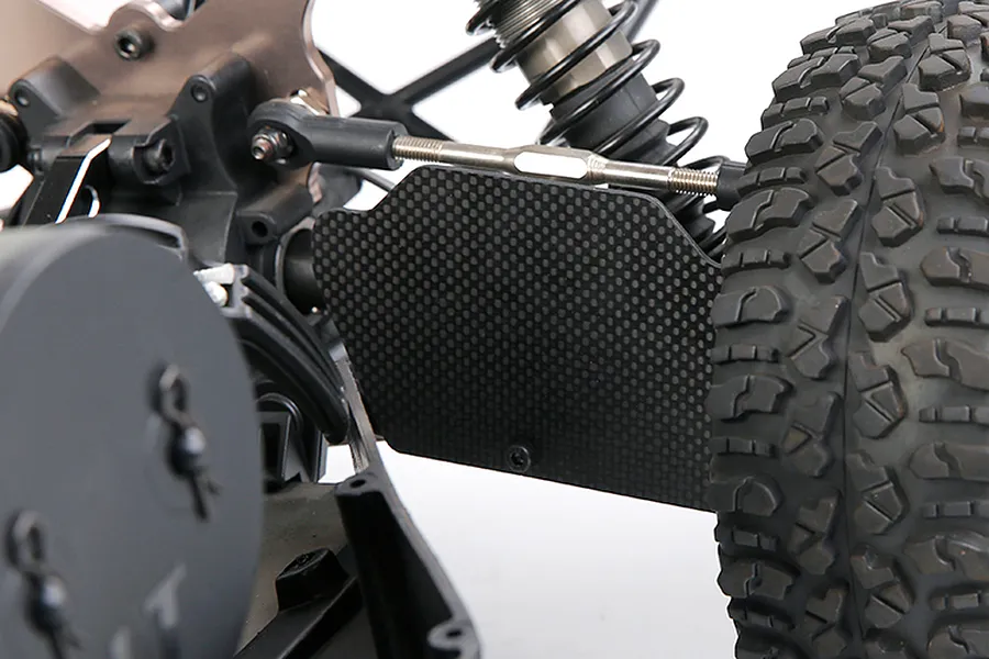 A close-up view of a carbon fibre rear suspension arm guard installed on an RC vehicle, showing the weave pattern and mounting position.