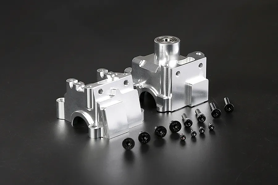 Two silver aluminium RC gearbox case halves and a set of black mounting screws arranged on a dark background.
