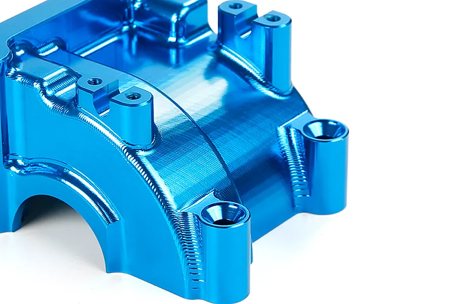 A close-up of a blue anodized aluminium RC gearbox case showing machined surfaces and mounting points.