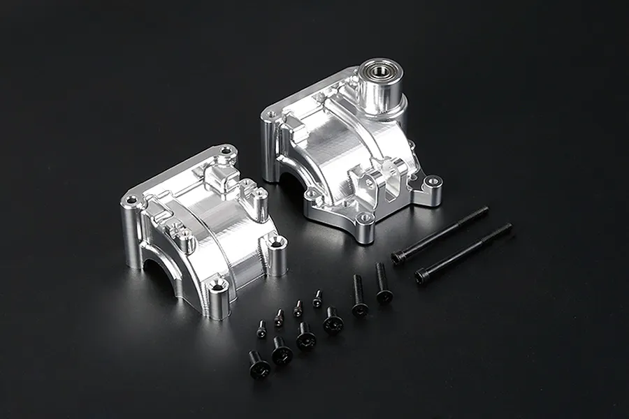 Two silver aluminium gearbox case halves and a set of black mounting screws on a dark background.