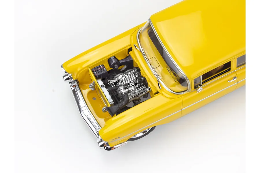 High-angle view of a yellow 1957 Chevrolet Bel Air model car with the hood open, revealing a detailed chrome engine bay.