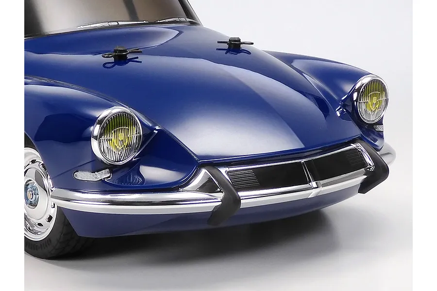 Close-up of the front end of a blue Tamiya Citroen DS RC car model, showing the hood, chrome bumper, and yellow-tinted headlights.