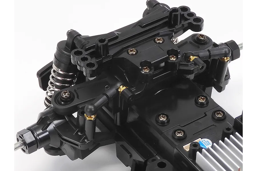 Close-up of the front suspension and chassis assembly of a Tamiya MB-01 RC car kit on a white background.