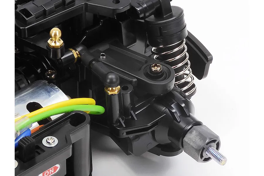Close-up view of the Tamiya MB-01 chassis front suspension assembly, showing black plastic arms, a coil-over shock, and steering linkage.