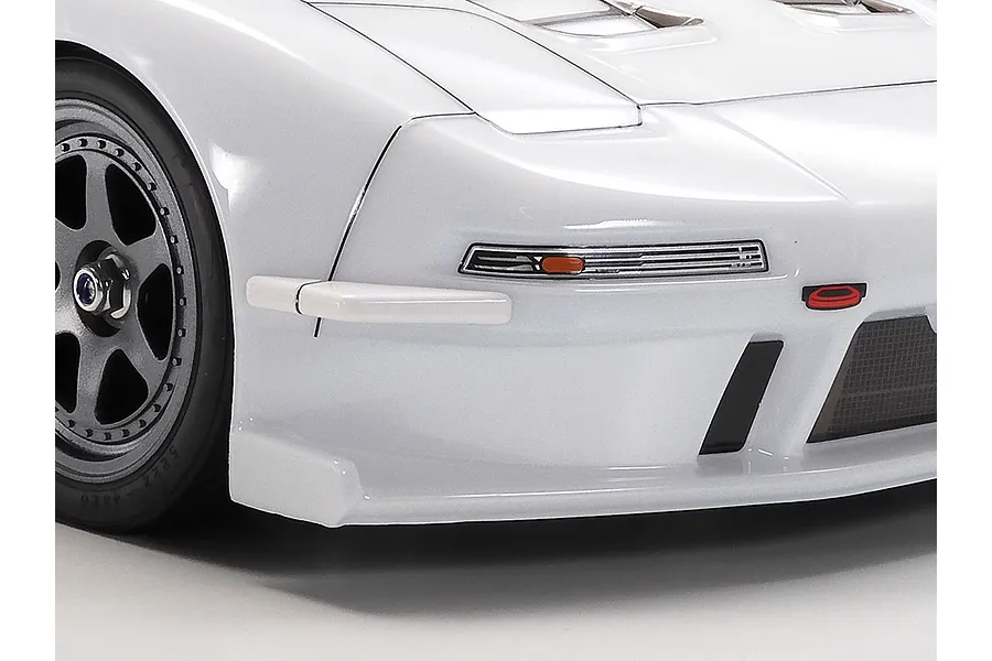 Close-up of the front left corner of a white Tamiya 1998 Honda NSX RC car body showing the wheel, bumper, and headlight detail.
