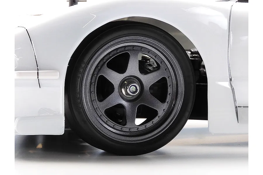 Close-up of the front wheel and white bodywork of a Tamiya 1/10 scale RC car.
