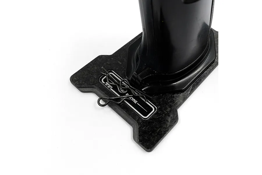 A close-up of a carbon fibre base plate for an RC transmitter, featuring a Yeah Racing logo and two metal body clips resting on the surface.