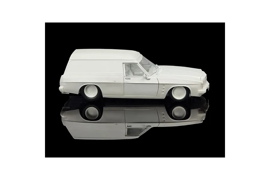 A side profile view of an unpainted white 1/24 scale 1975 Holden HJ Panelvan model kit on a reflective black surface.