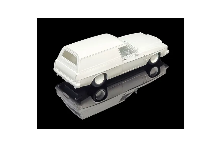 A high-angle studio shot of an unpainted white plastic model kit of a 1975 Holden HJ Panelvan, shown on a black reflective surface.