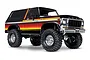 A studio shot of a black Traxxas TRX-4 Ford Bronco Ranger XLT RC rock crawler with red and yellow side stripes, chrome wheels, and large off-road tires.