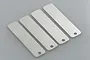 Four rectangular metal feeler gauge strips with rounded corners and a hole at one end, arranged diagonally on a grey background.