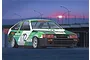 Box art illustration of a green and white Toyota AE86 Levin race car with Trampio livery parked at a track during sunset.