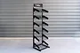 A black metal Koswork floor display rack with six angled wire shelves for organizing products.