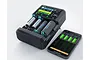 SkyRC MC5000 smart battery charger with four cylindrical batteries inserted, shown next to a smartphone displaying the charger's app interface.