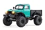 A green FMS FCX24 Power Wagon RC rock crawler truck with black fenders and bed, featuring illuminated headlights against a white background.