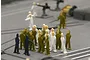 A group of small, unpainted plastic miniature figures representing ship crew members standing on a grey model ship deck.