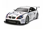 A Tamiya 1/10 scale RC BMW M3 GT2 race car model with white body, blue and red racing stripes, and sponsor decals on a white background.