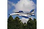 E-Flite Habu SS RC jet plane flying against a blue sky with clouds and trees in the background.