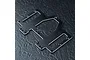 A black anodized aluminium battery and servo mounting plate for an RC car, featuring multiple screw holes and cutouts, resting on a dark textured surface.