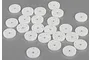 A collection of twenty-four white plastic RC shock pistons scattered on a grey surface.