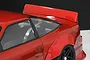 Close-up of a red RC car body featuring a ducktail spoiler mounted on the rear decklid and wide fender flares.