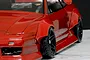 Close-up of a red RC car body installed with wide over fender flares and black wheels on a marble surface.