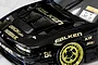 Close-up of a black RC drift car body with gold decals, custom vented hood, and gold rims on a light surface.