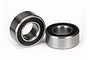 Two small metal ball bearings with black rubber seals sitting on a white surface.