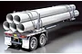 A Tamiya 1/14 scale RC pole trailer model loaded with large grey pipes secured by metal chains against a black background.