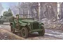 Box art illustration of a green Soviet GAZ-67B military staff car driving past a tank through a ruined city street.