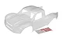 A clear, unpainted polycarbonate body shell for the Traxxas Unlimited Desert Racer RC truck, shown with an included sheet of Traxxas logo decals.