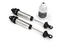 Two assembled silver aluminium Traxxas GTR shocks for the UDR with a small bottle of silicone shock oil on a white background.