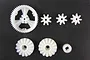 A set of six white plastic differential gears of various sizes arranged on a dark background.