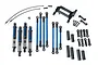 Traxxas TRX-4 long arm lift kit components including blue anodized shocks, suspension links, and black plastic mounting hardware on a white background.
