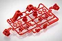A red plastic Tamiya parts tree containing various RC car suspension components, including hubs and mounts, on a white background.
