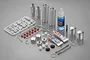 A Tamiya silver aluminium shock absorber kit including metal shock bodies, springs, oil, grease, and various plastic and rubber components on a grey background.