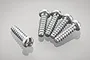 Five silver metal binder head screws with coarse threads arranged on a reflective white surface.