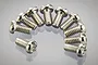 A collection of ten small silver-coloured metal binder head screws arranged in a semi-circle on a reflective grey surface.