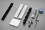 Tamiya Frog hardware and tool set including grease, hex wrenches, a cross wrench, rubber bellows, and adhesive foam strips on a grey background.