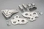 A collection of Tamiya Frog metal pressed chassis parts including gearbox plates, suspension mounts, and a small black plate on a grey background.